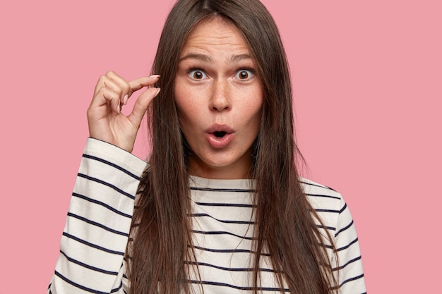 Size concept. Close up shot of amazed attractive female shapes small object with hand