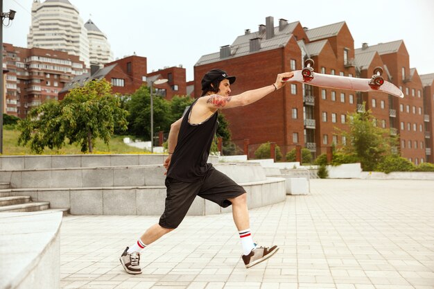 Skateboarder doing a trick at the city's street in cloudly day. Young man in sneakers and cap riding and longboarding on the asphalt. Concept of leisure activity, sport, extreme, hobby and motion.