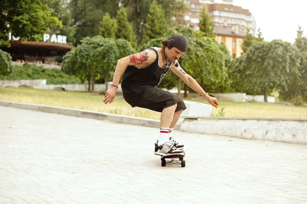 구름이 많은 날에 도시의 거리에서 트릭을하는 스케이트 보더. 운동화와 모자를 타고 아스팔트에 longboarding 젊은 남자. 여가 활동, 스포츠, 익스트림, 취미 및 운동의 개념.