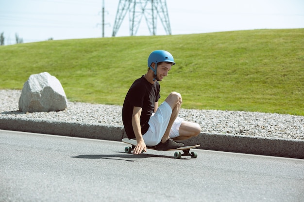 Free photo skateboarder doing a trick at the city's street in sunny day. young man in equipment riding and longboarding on the asphalt in action. concept of leisure activity, sport, extreme, hobby and motion.