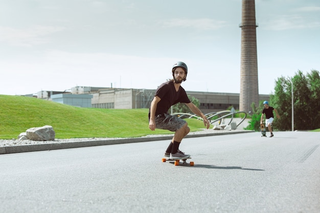 Скейтбордист делает трюк на улице города в солнечный день. Молодой человек в снаряжении верховой езды и лонгбординга на асфальте в действии. Концепция досуга, спорта, экстрима, хобби и движения.