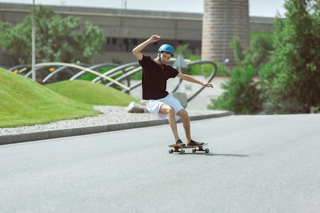 Skateboarder doing a trick at the city's street in sunny day. Young man in equipment riding and longboarding on the asphalt in action. Concept of leisure activity, sport, extreme, hobby and motion.