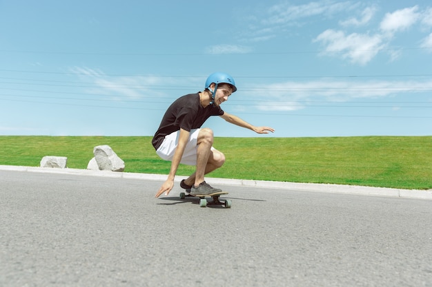 Skateboarder doing a trick at the city's street in sunny day. Young man in equipment riding and longboarding near by meadow in action. Concept of leisure activity, sport, extreme, hobby and motion.