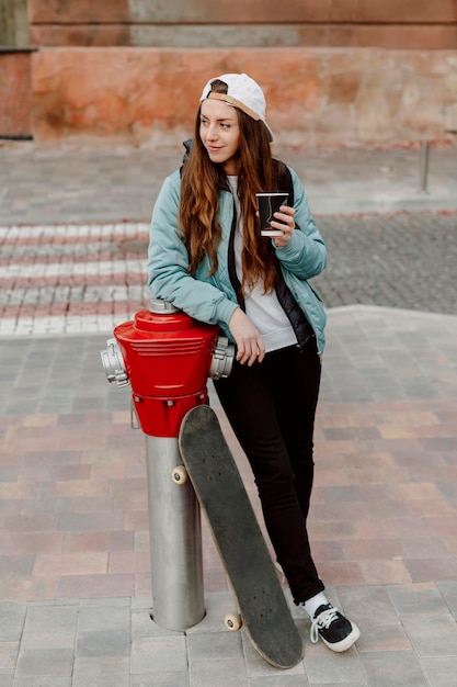 Foto gratuita ragazza del skateboarder che tiene una tazza di caffè uno sguardo lontano