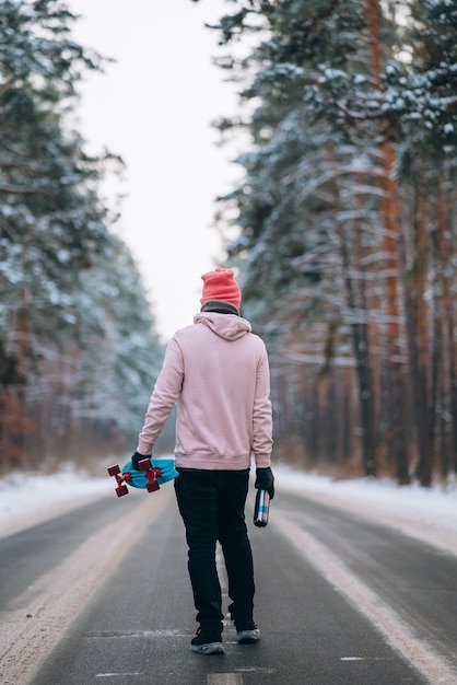 Скейтбордист, стоящий на дороге посреди леса в окружении снега