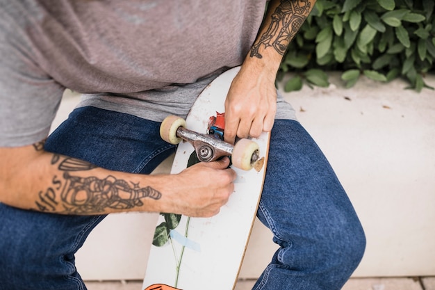 Skateboarder with tattoo on his hand fixing wheels of skateboard