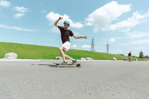 Skateboarders doing a trick at the city's street in sunny day. Young men in equipment riding and longboarding on the asphalt in action. Concept of leisure activity, sport, extreme, hobby and motion.