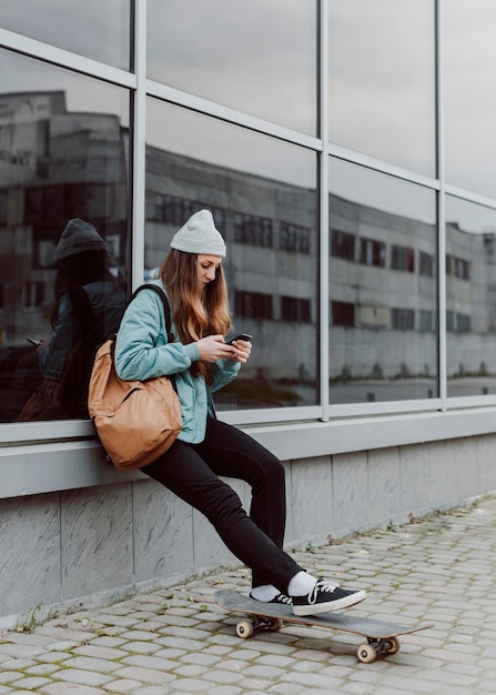 Foto gratuita ragazza pattinatrice nella seduta urbana accanto a un edificio