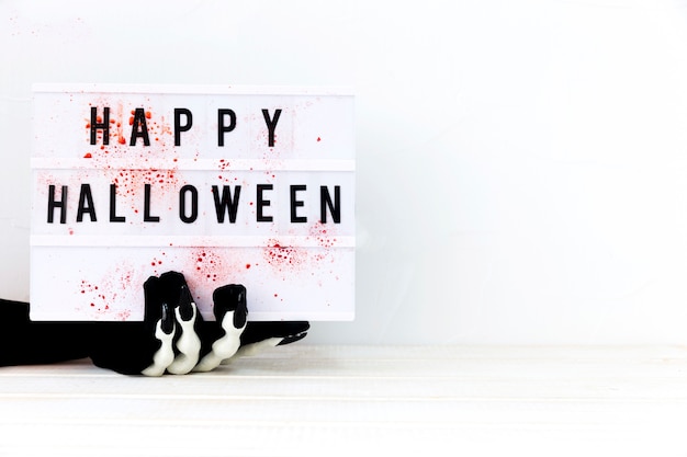 Skeleton hand holding board with Happy Halloween writing