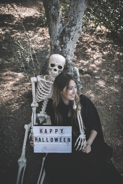 Skeleton hugging smiling lady with tablet in dark clothes