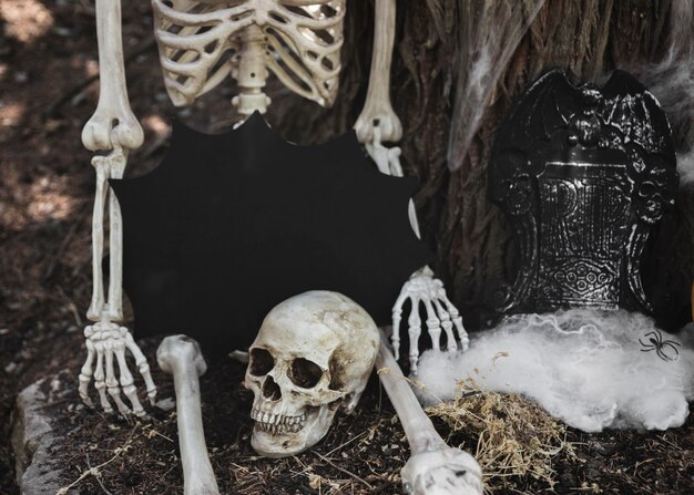 Skeleton with tablet in blot form sitting near tombstone leaning on tree