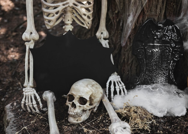 Скелет с таблеткой в ​​блот-форме, сидя возле надгробия, опираясь на дерево