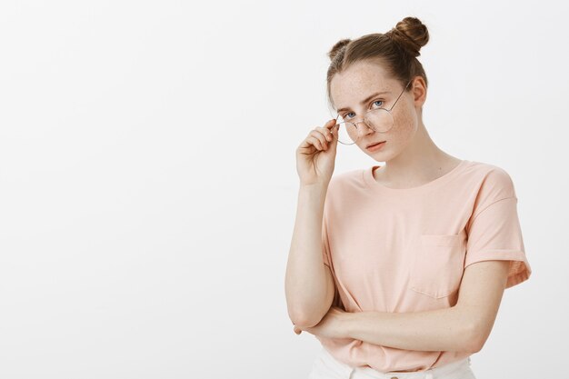 Skeptical arrogant redhead teenage girl posing against the white wall