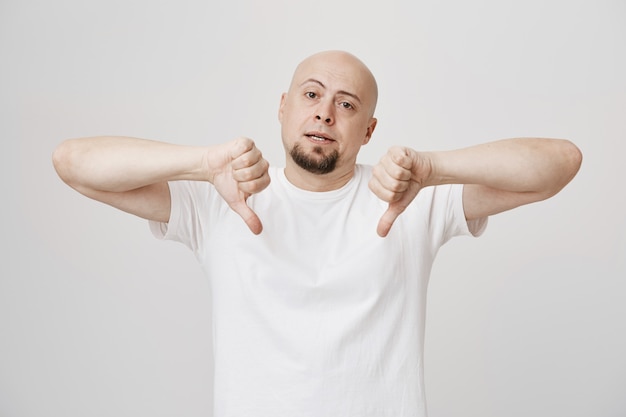 Free photo skeptical bald bearded guy show thumbs-down being disappointed
