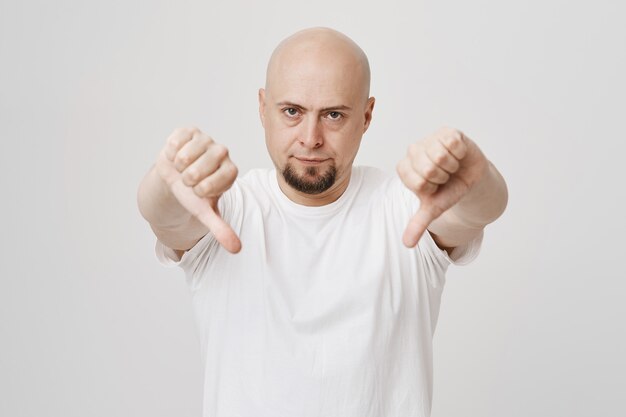 Skeptical bald bearded guy show thumbs-down in dislike