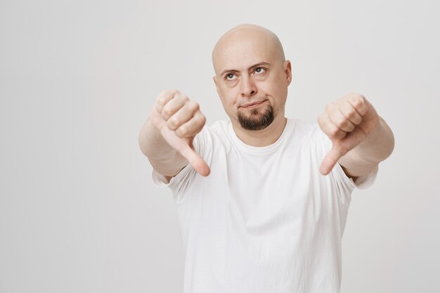 懐疑的なハゲのひげを生やした男は親指を下にして目を丸める