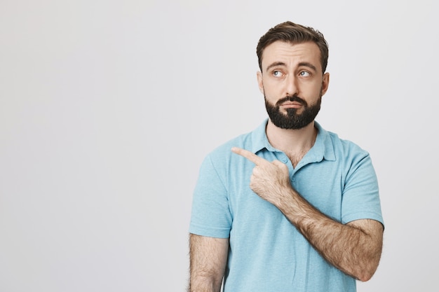 Free photo skeptical bearded man looking and pointing left unimpressed