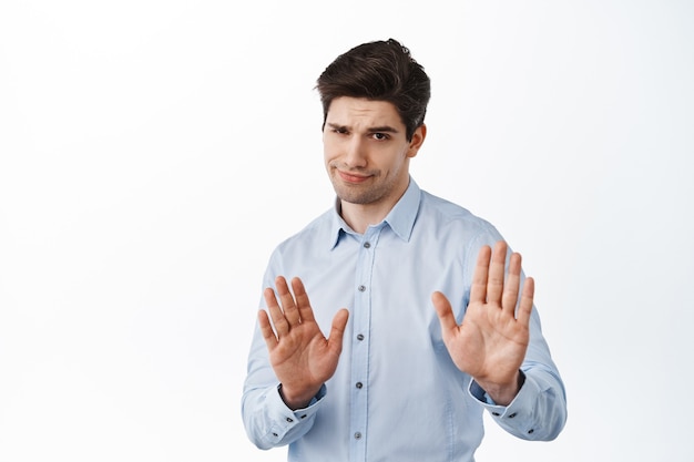 Free photo skeptical boss, male entrepreneur showing refuse, reject block gesture, telling to quit, standing over white wall
