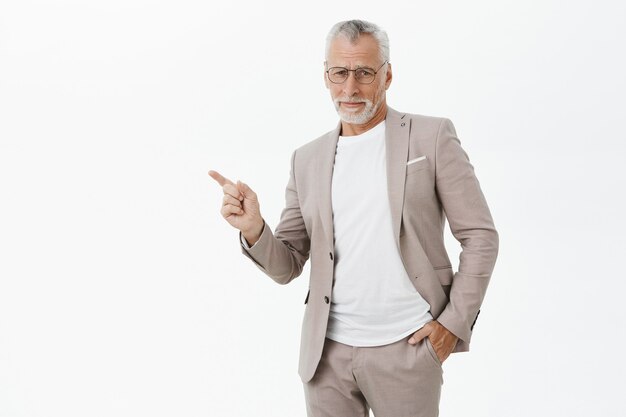 Skeptical businessman in suit and glasses pointing finger left doubtful