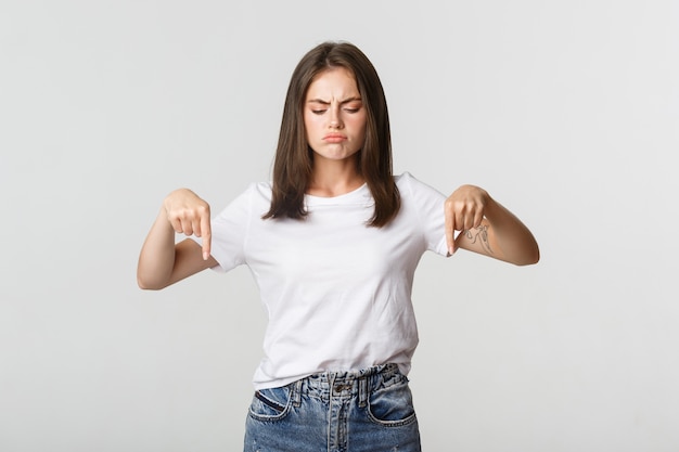 Skeptical or disappointed brunette girl complaining, pointing fingers down.