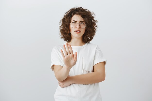 Skeptical and disappointed woman showing stop gesture and cringe from dislike, refuse, rejecting offer