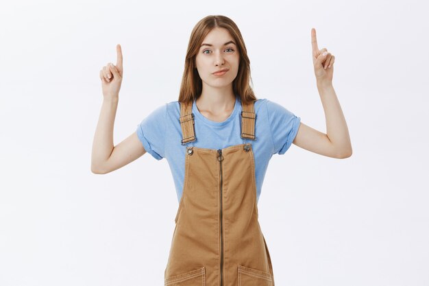 Скептическая и недовольная девушка, указывающая пальцем на логотип или рекламу