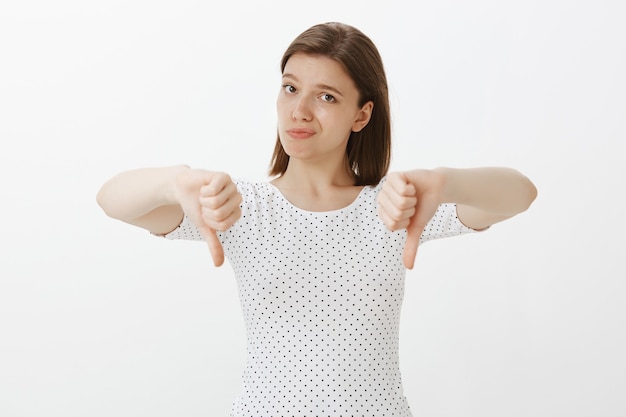 Skeptical and displeased woman showing thumbs-down in disapproval, dislike idea