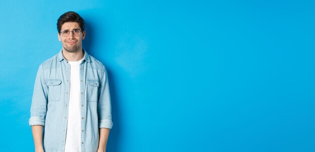 Skeptical and doubtful guy in glasses looking confused at something strange blue background