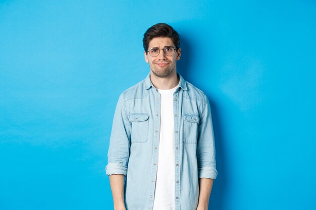 Skeptical and doubtful guy in glasses, looking confused at something strange, blue background