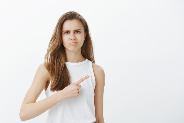 Skeptical and judgemental girl don't recommend product, pointing right and grimacing disappointed