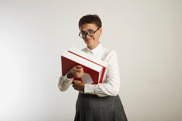 Skeptical looking conservatively clothed female teacher holding heavy bright binders on white