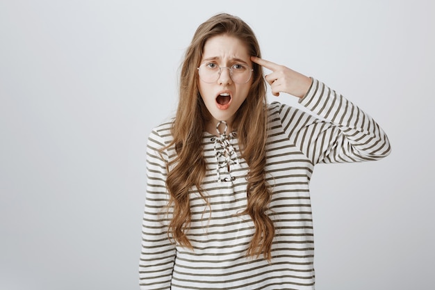 Free photo skeptical nerdy girl pointing at temple as scolding person acting stupid