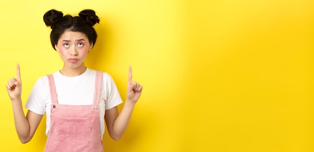 무료 사진 글램 핑크 메이크업을 가리키며 즐겁지 않은 서 있는 relucta를 올려다보는 회의적인 10대 아시아 소녀