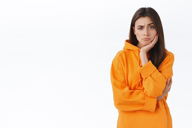 Skeptical and unamused brunette girl hear friends suggestion looking judgemental and doubtful at camera with raised eyebrow express disbelief lean face on hand standing white background