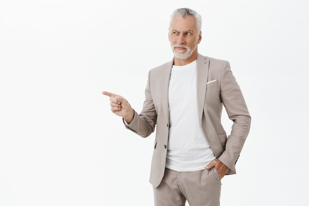 Skeptical and unsure businessman in suit pointing finger left and grimacing