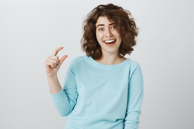 Skeptical woman making fun of small size, showing something tiny or little
