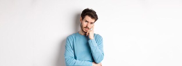 Skeptical young man listening to you with bored face looking at camera reluctant standing in sweatsh