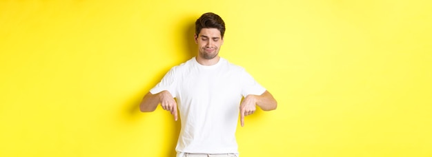 Skeptical young man in white tshirt pointing and looking down upset disapprove and dislike product s