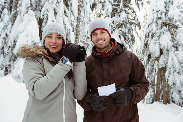 Skier couple holding a binocular and address card on snow covered mountain