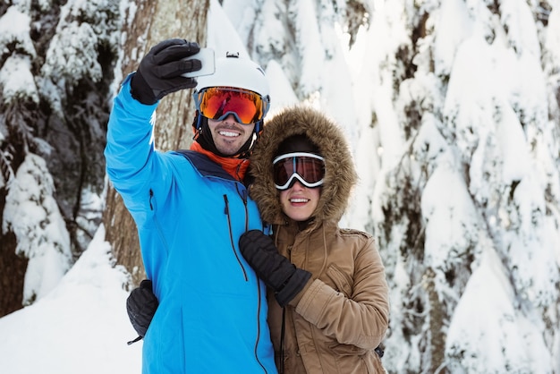 雪景色で自分撮りをしているスキーヤーのカップル