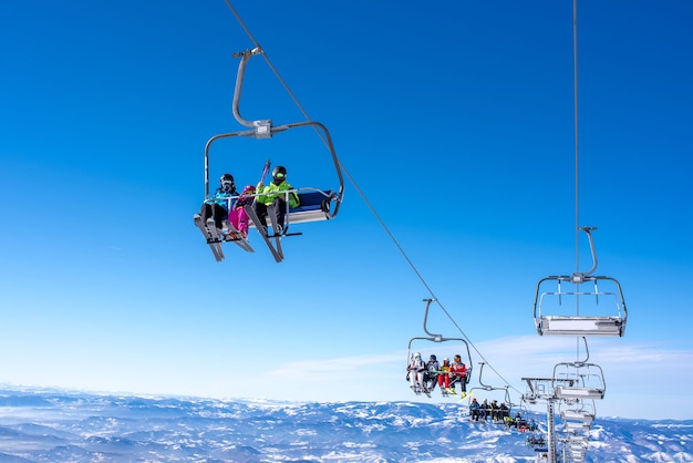 Skiers on a ski lift at a mountain resort with the sky and mountains in the background