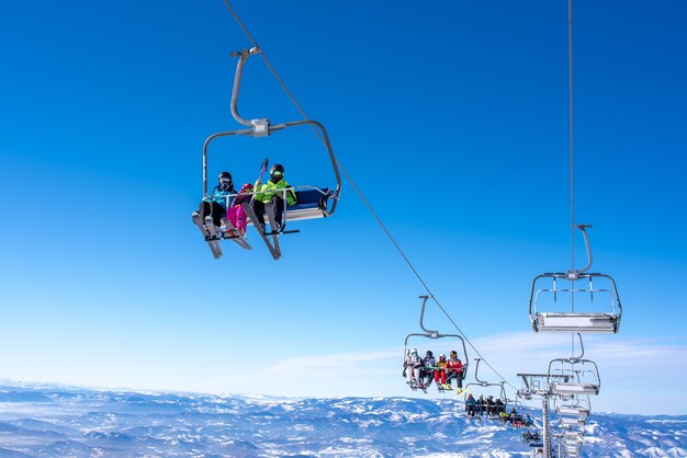 하늘과 산을 배경으로 한 산악 리조트에서 스키 리프트를 타는 스키어들