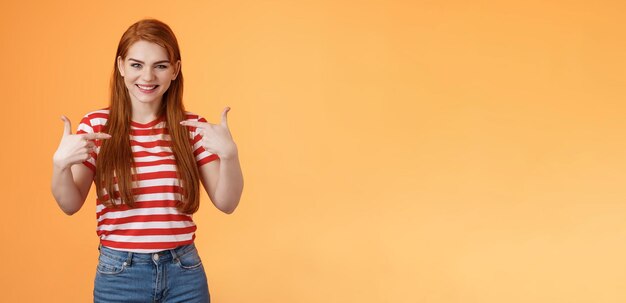 巧みな見栄えの良い赤毛の意欲的な女の子が自分自身を指さし、指の胸を喜んで自慢している