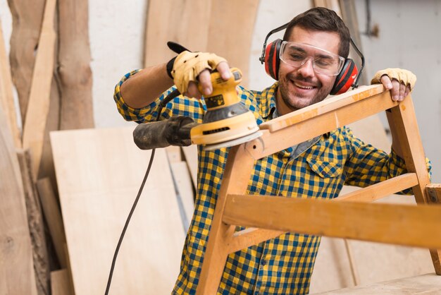 A skilled carpenter is using the power sander as a tool to polish his furniture