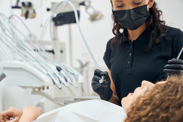 Skilled dentist in uniform and mask curing teeth of patient