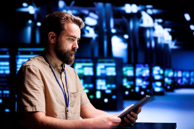 Skilled mechanic resolving performance related issues in server room. Expert utilizing tablet to identify operational problems causing high tech facility electronics slowdown