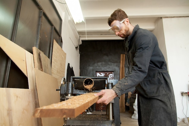 Skilled worker processing wooden flooring plank on woodworking power planer