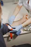Foto gratuita l'infermiera abile sta facendo l'analisi del sangue per l'uomo in clinica. uomo in una maschera medica.