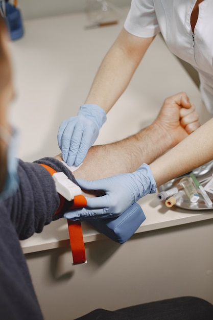 Skillful nurse is doing blood test for man in clinic. Man in a medical mask.