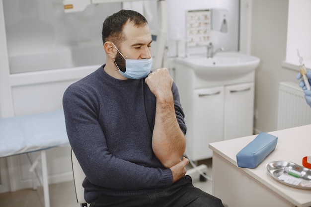 Skillful nurse is doing blood test for man in clinic. Man in a medical mask.